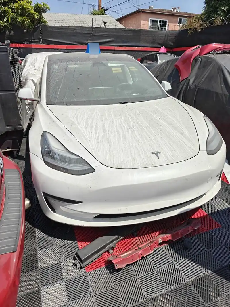 White Tesla Model 3 parked in a repair bay with front bumper parts on the floor